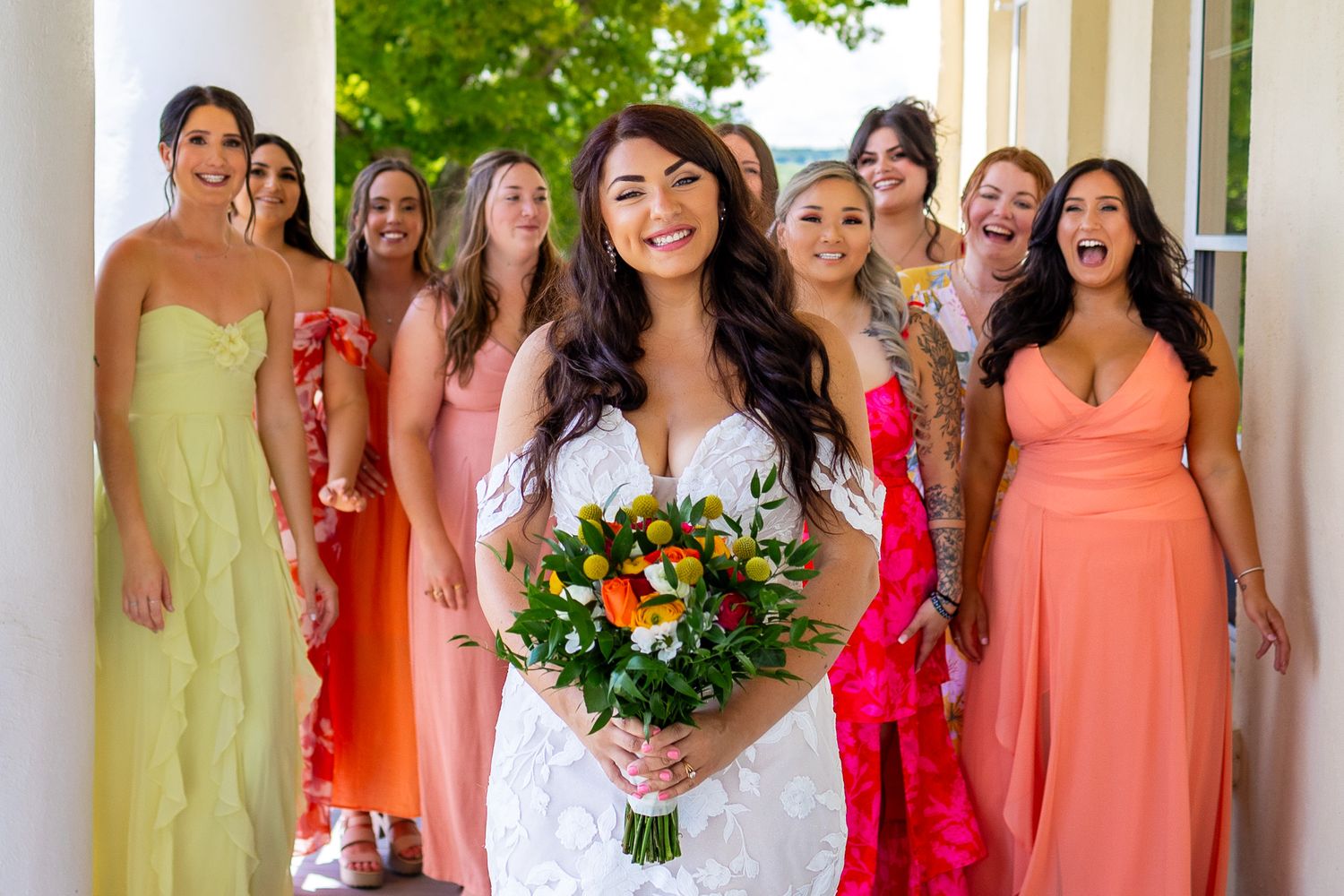 Bridal party in colorful dresses poses on white columned porch.