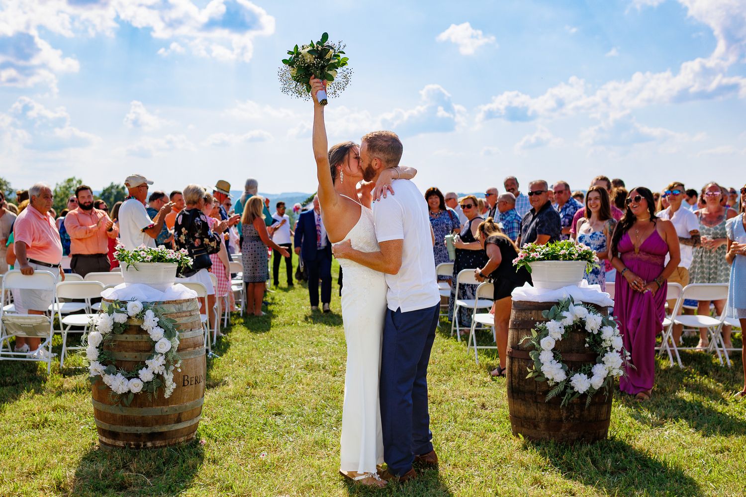 A series of outdoor wedding ceremony photos showing guests seated in white chairs on a grassy hillside under blue skies.