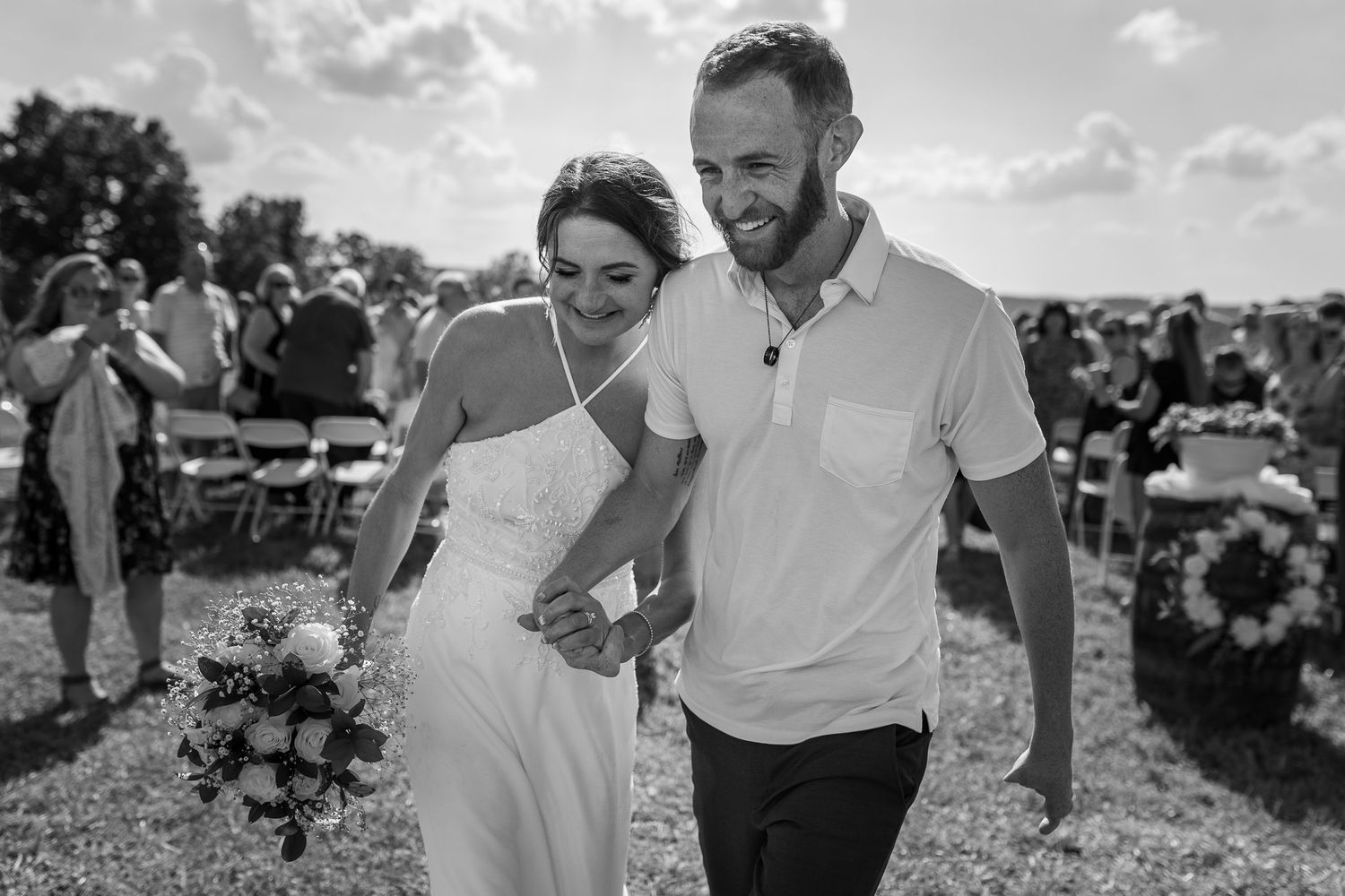 A couple laughs and runs together through a sunny outdoor field during a joyful moment.