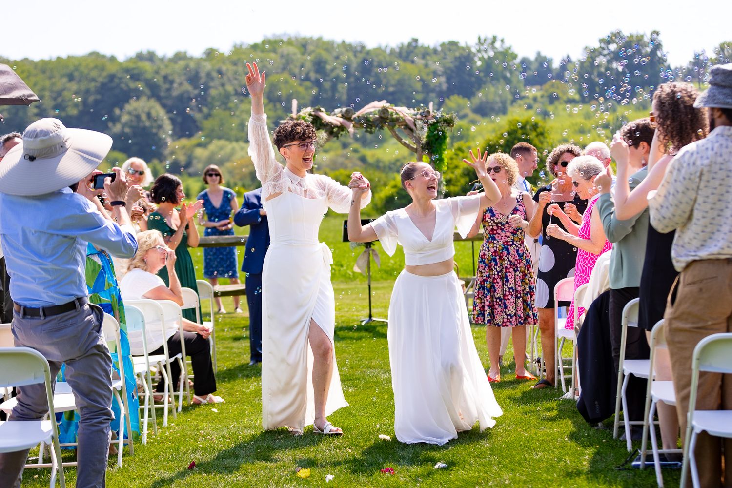 Wedding celebration on lawn with guests cheering and couples raising arms in celebration.