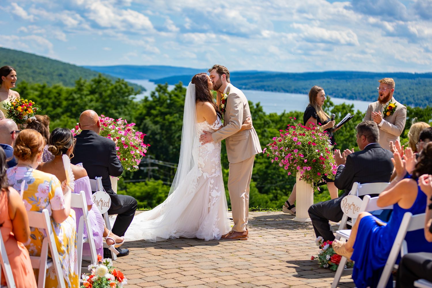 Outdoor wedding ceremony overlooking scenic lake vista with guests in attendance.