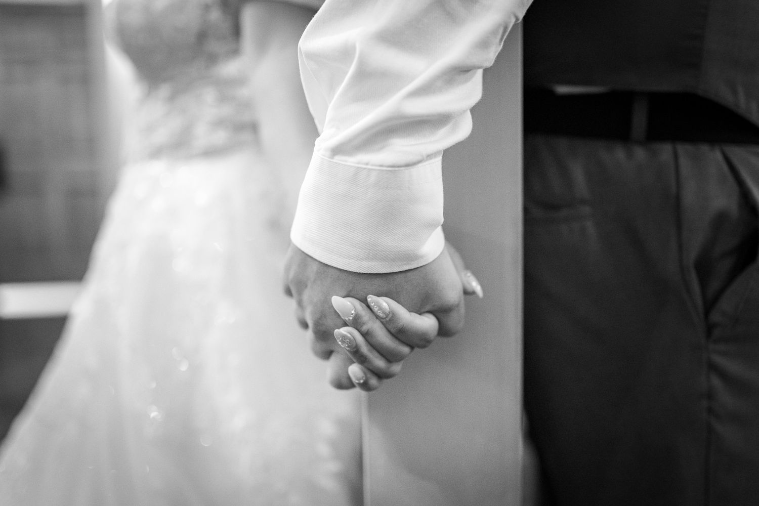 A black and white close-up photograph of a bride and groom holding hands during their wedding ceremony.