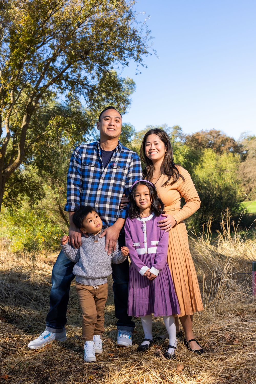 Family of four poses together under trees during a fall outdoor photo session.