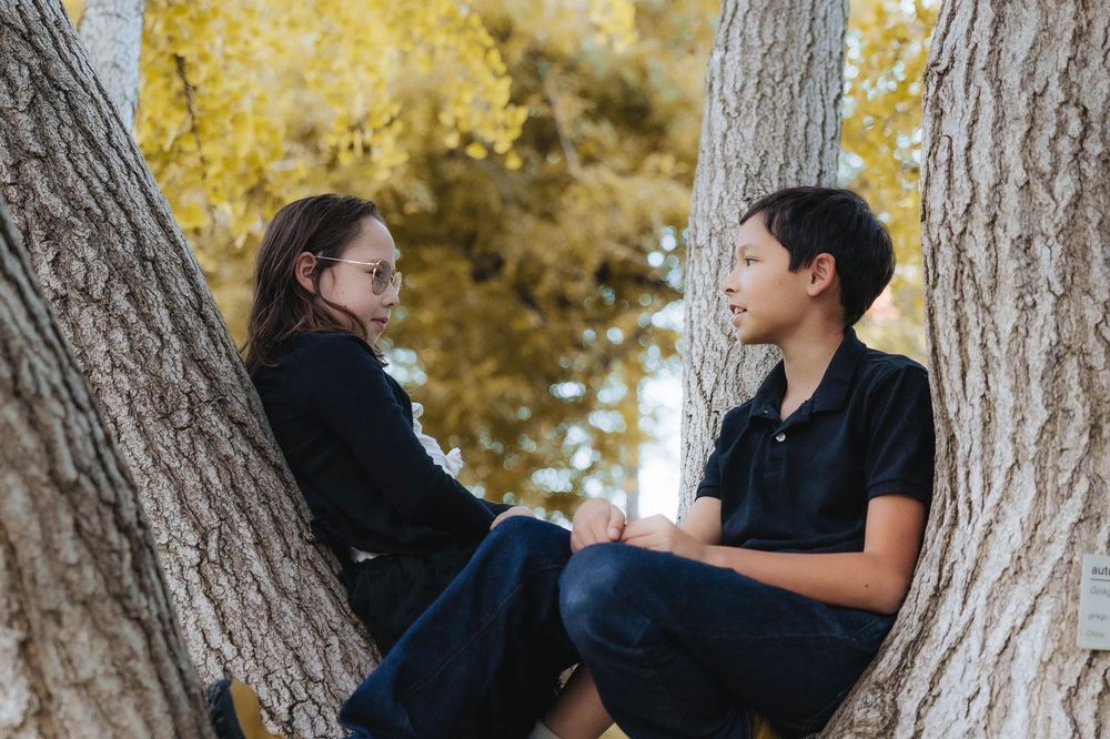 A couple shares a romantic moment between trees with golden autumn foliage in the background.