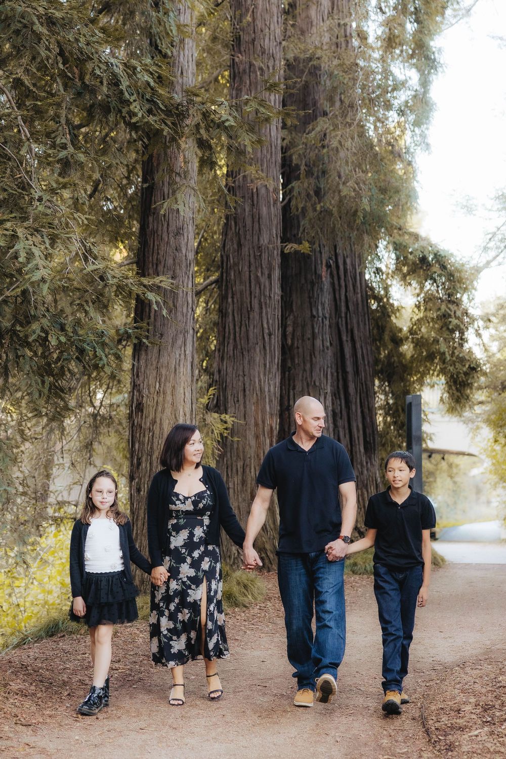 Family walking together on a tree-lined dirt path during golden hour at a park.