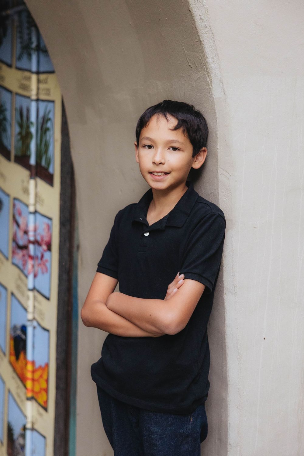 Child posing against a white wall with stained glass windows in casual black attire.
