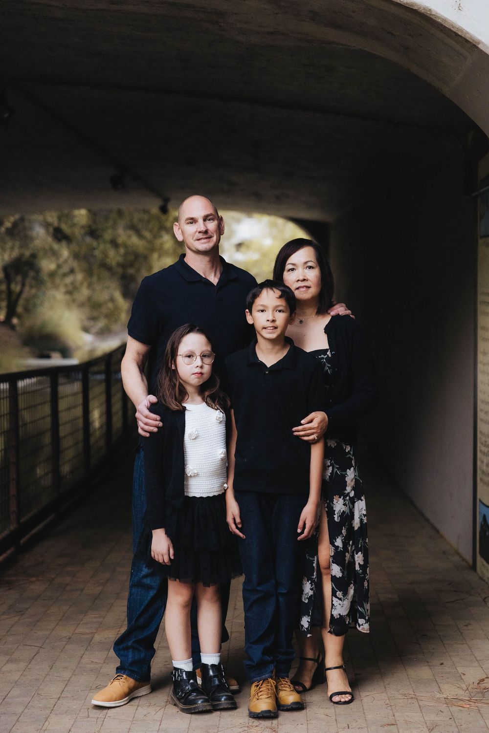A family stands together in a dark tunnel-like hallway with arched ceilings and tiled floors.