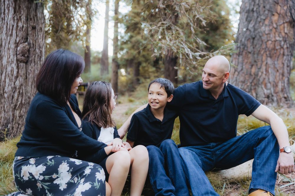 A series of candid family photos taken outdoors in a wooded setting with pine trees in the background.