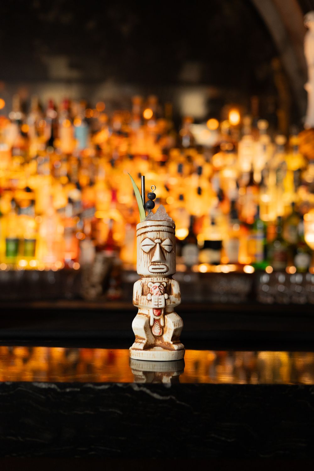 Tiki statue figurine displayed against a blurred backdrop of illuminated liquor bottles.