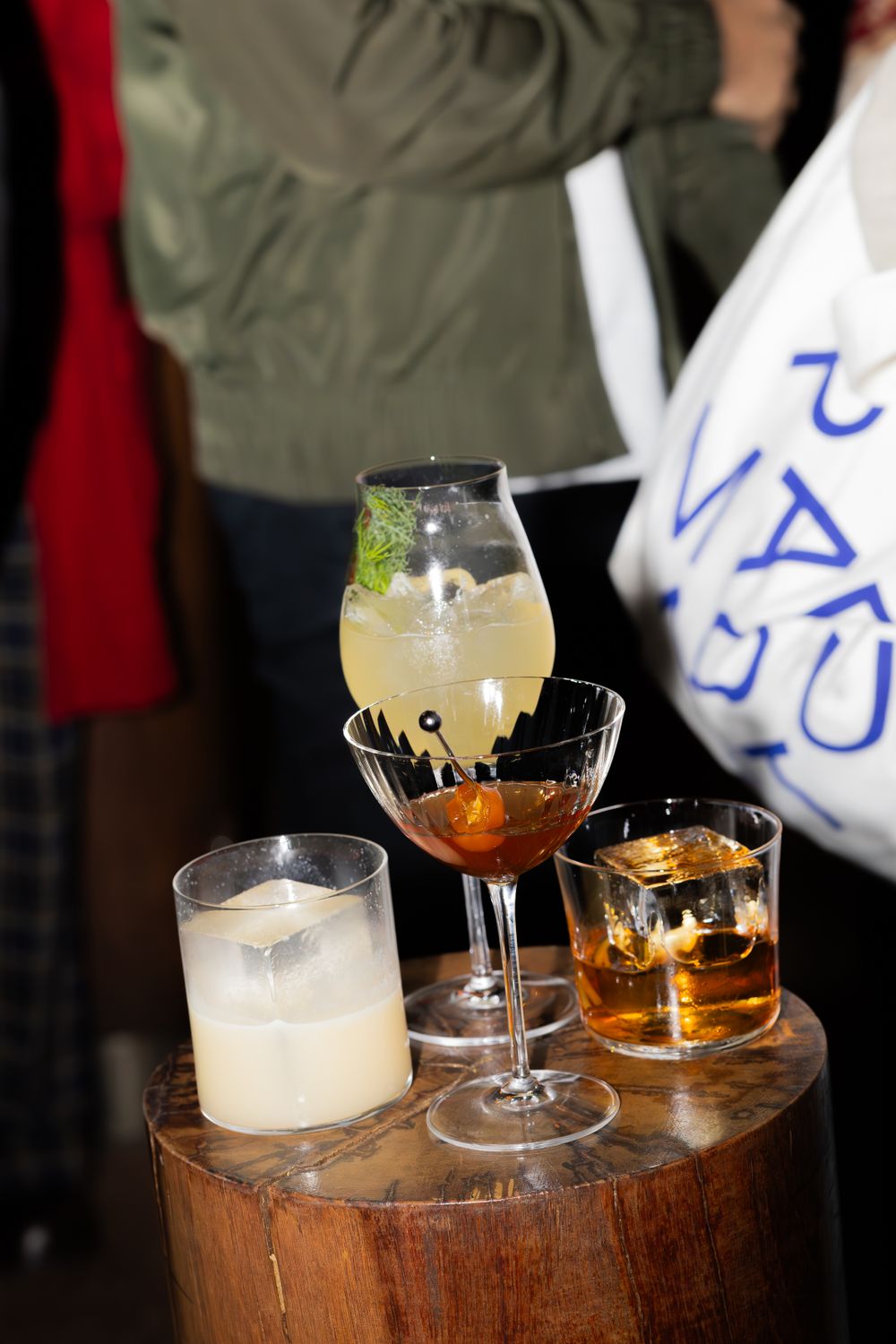 Assorted cocktails displayed on wooden barrel surface including clear and amber colored drinks.