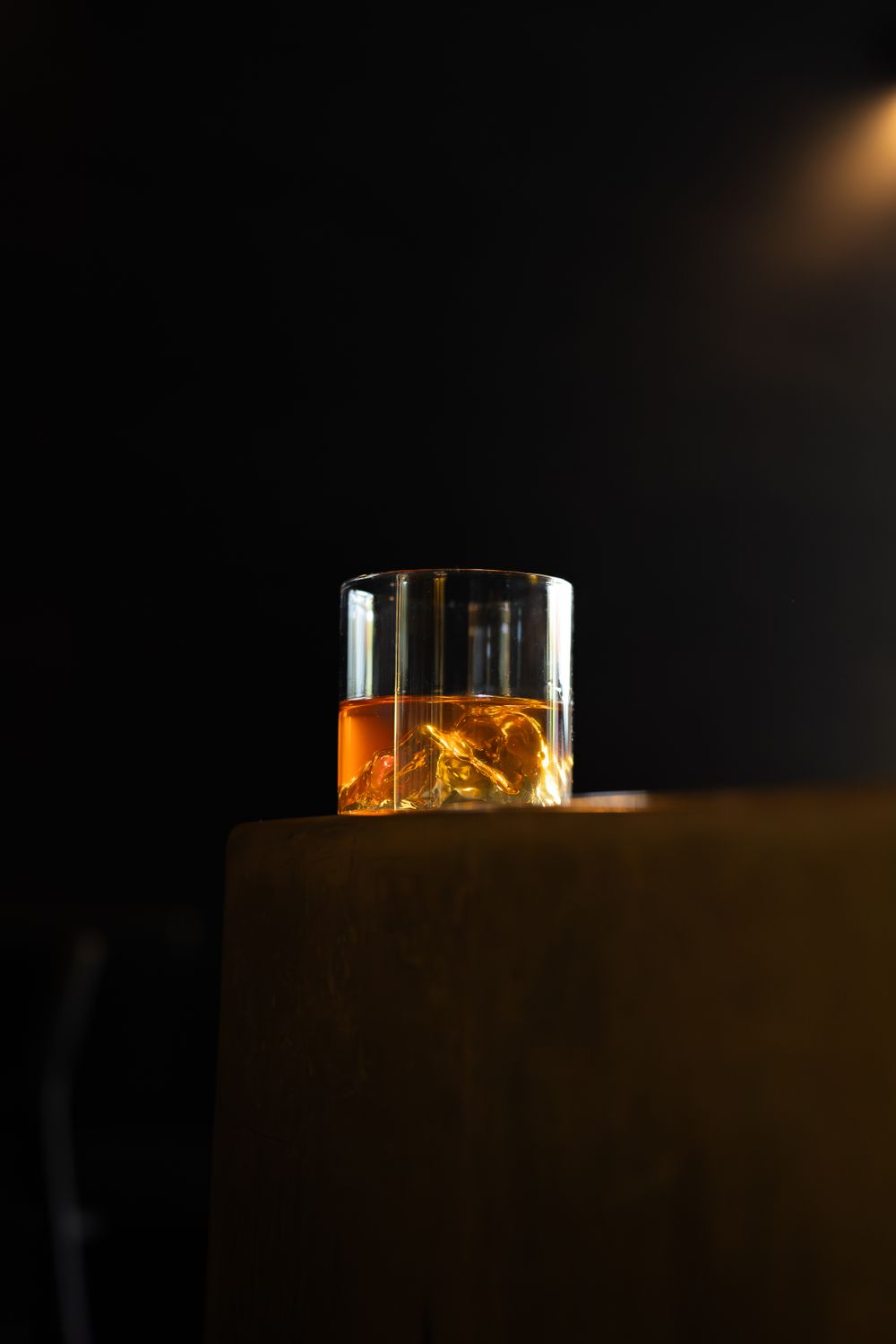 Whiskey glass with ice cubes illuminated dramatically against dark background.