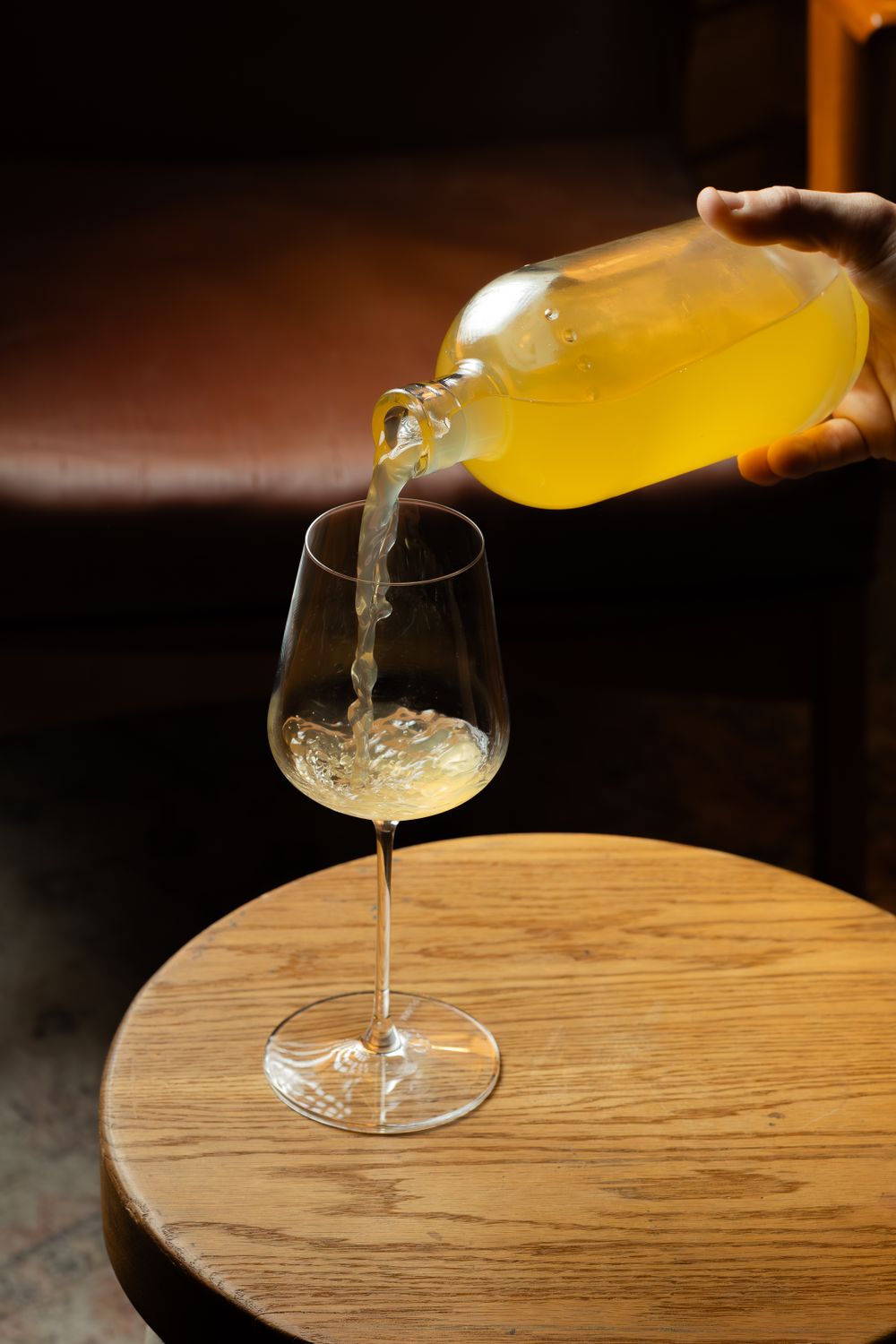 Golden liquid being poured from a bottle into a stemmed wine glass on wooden table.