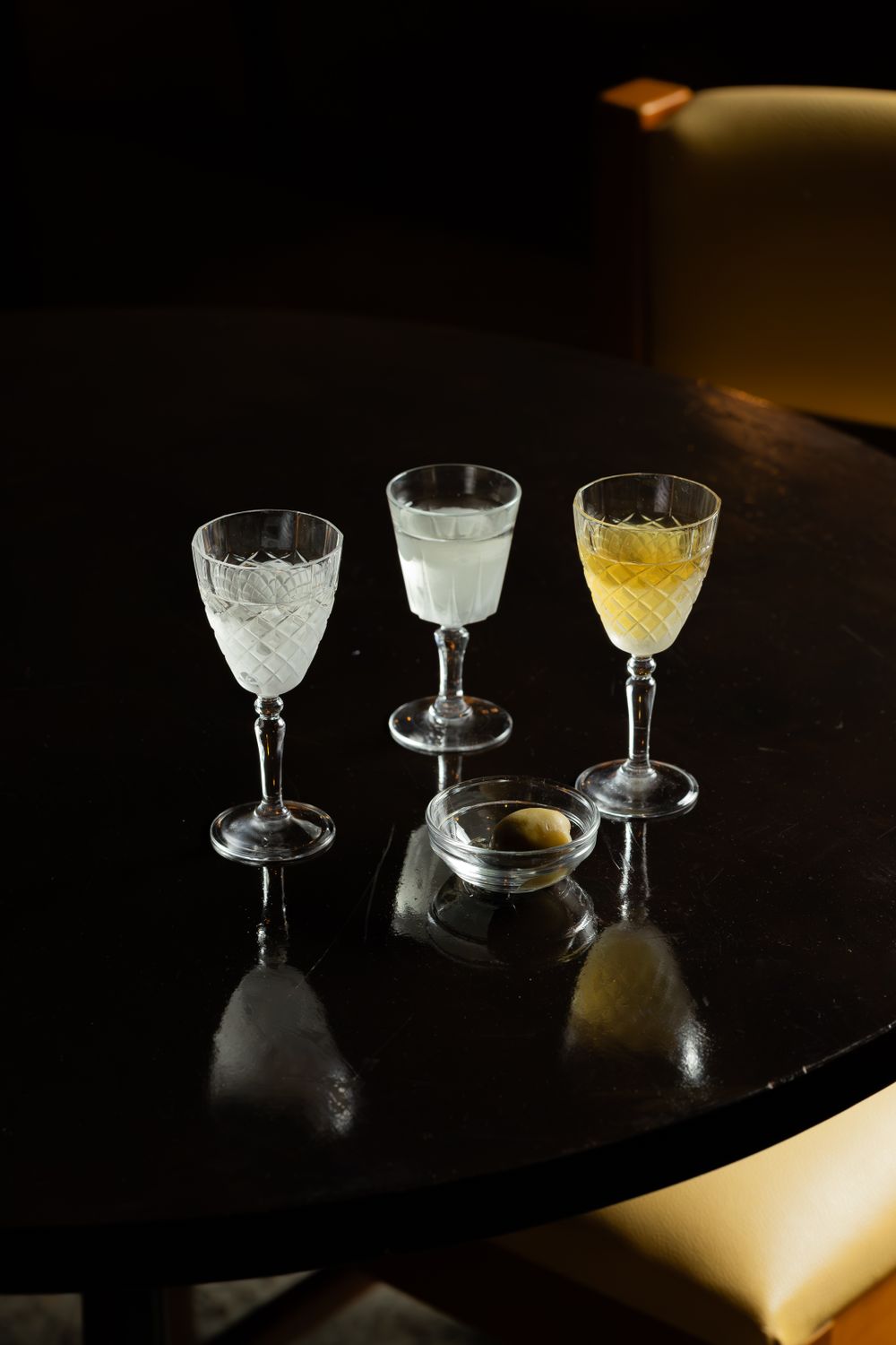 Three elegant cocktail glasses and a glass bowl arranged on a dark table with dramatic lighting.