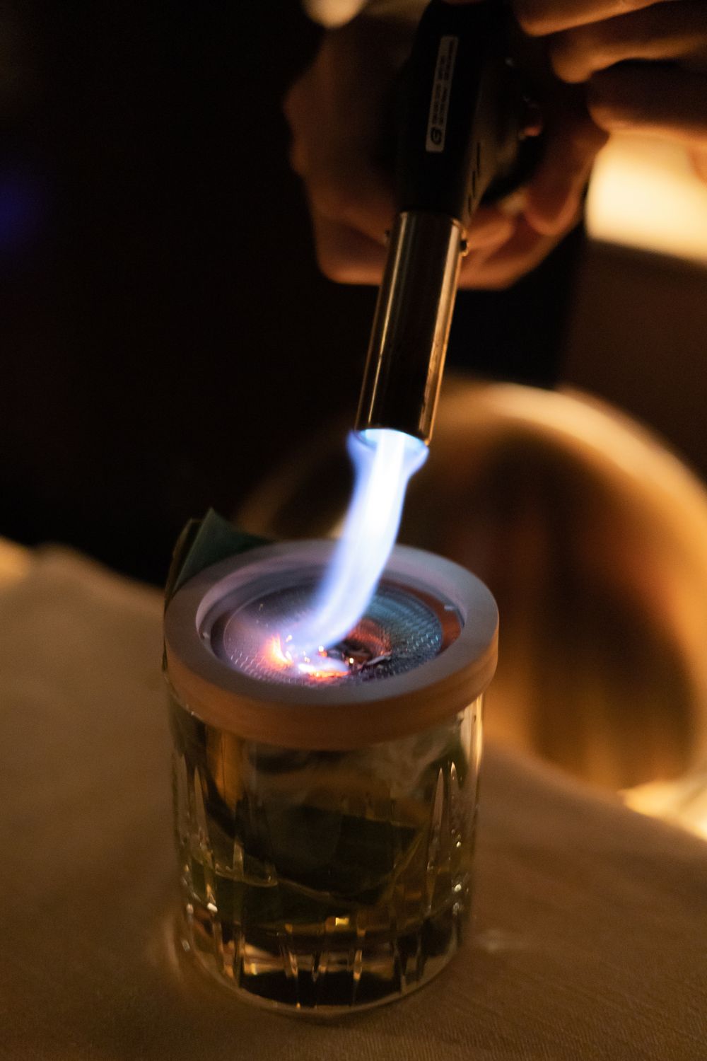 Flame being applied to cocktail with torch creating dramatic lighting effect.