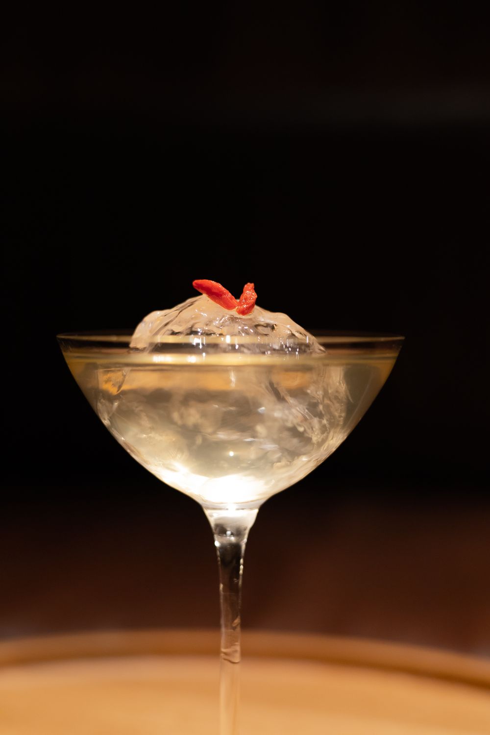 Elegant cocktail in coupe glass garnished with red flower and clear ice.