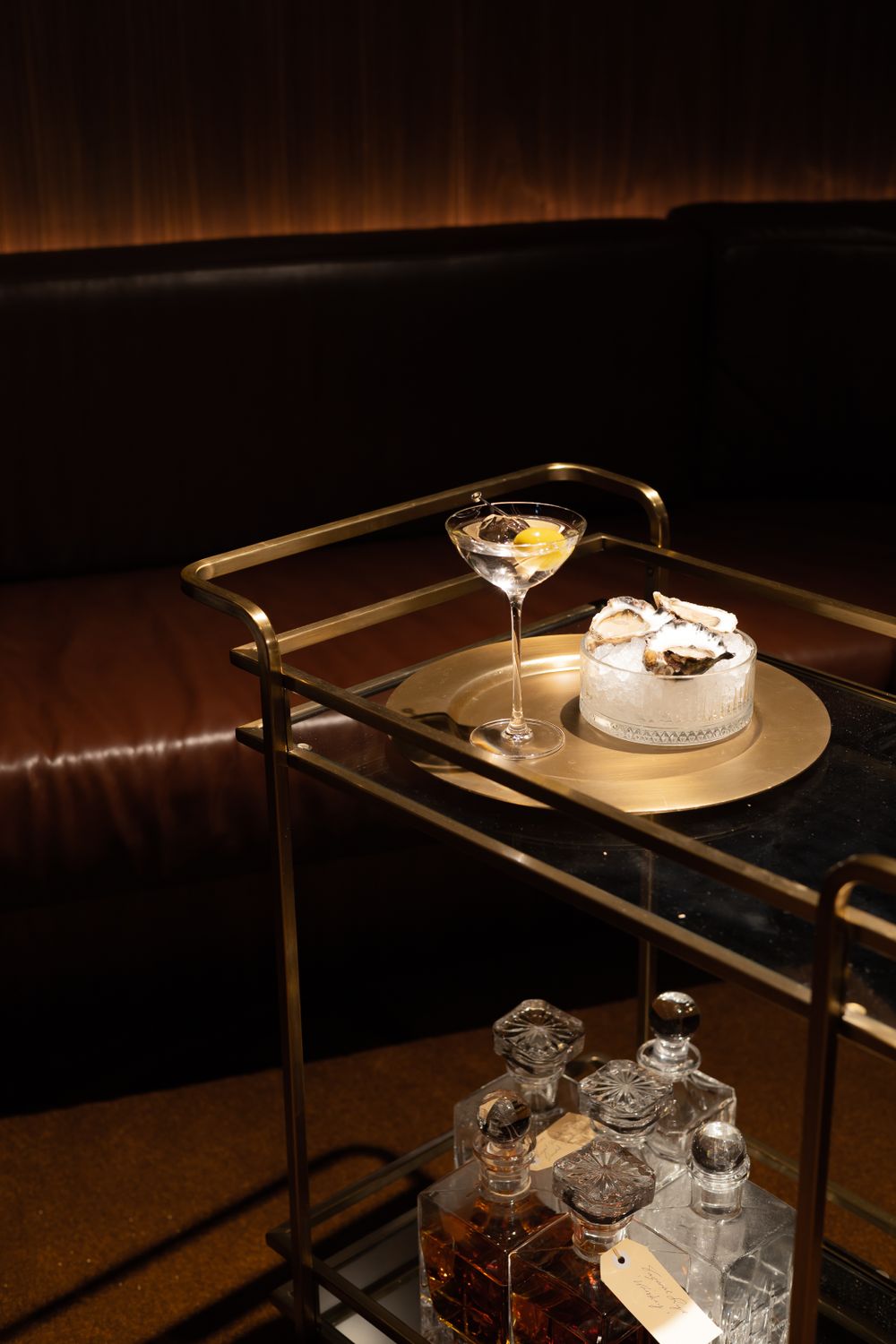 Bar cart with martini glass and dessert plate against dark leather banquette.