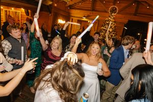 Wedding reception guests dance and celebrate with raised arms on a crowded dance floor under warm lighting.