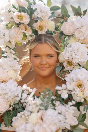 Ethereal floral portrait surrounded by delicate white blossoms and green foliage in soft, warm lighting.
