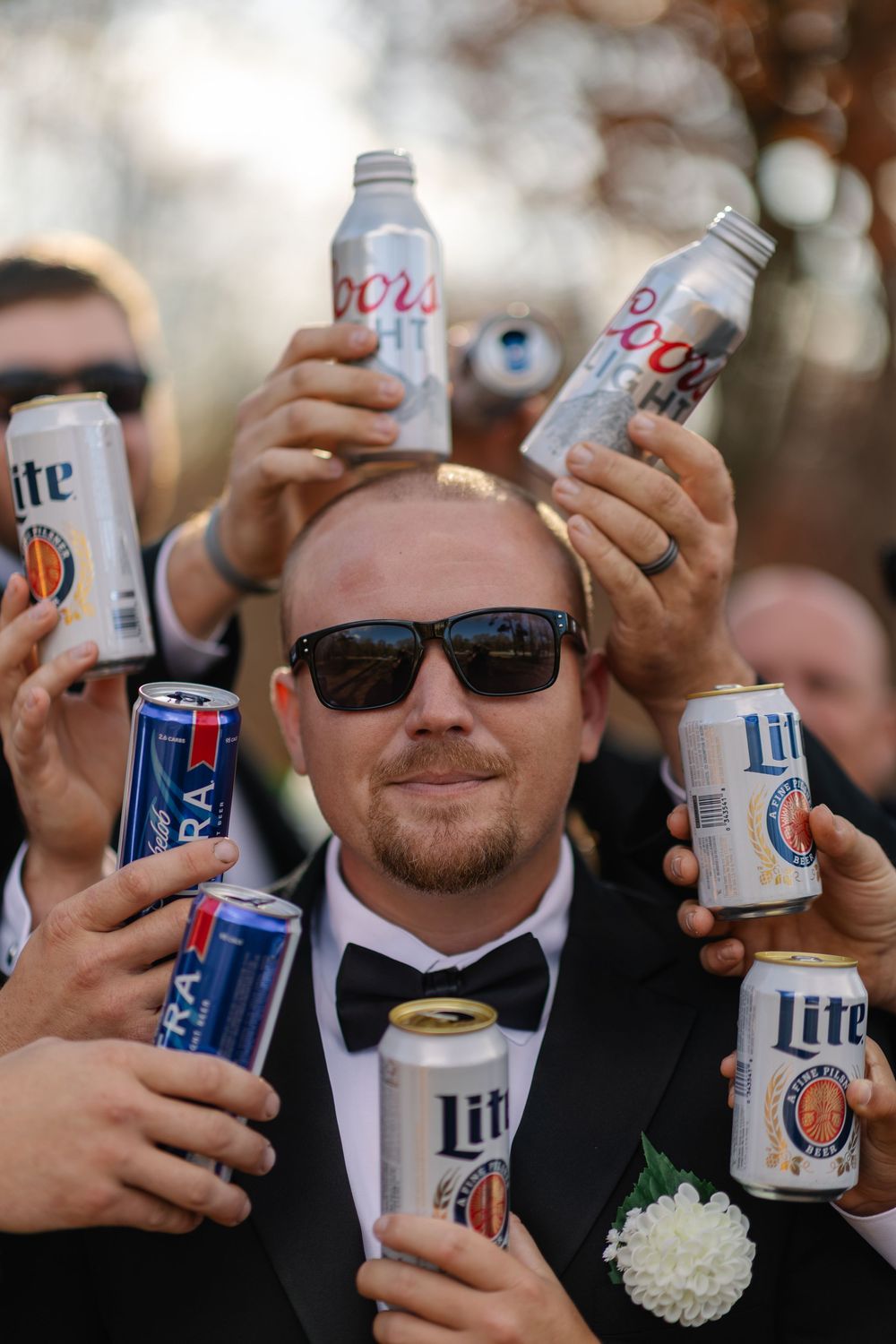 A group of hands holding up cans of beer in a celebratory toast during what appears to be a party or gathering.