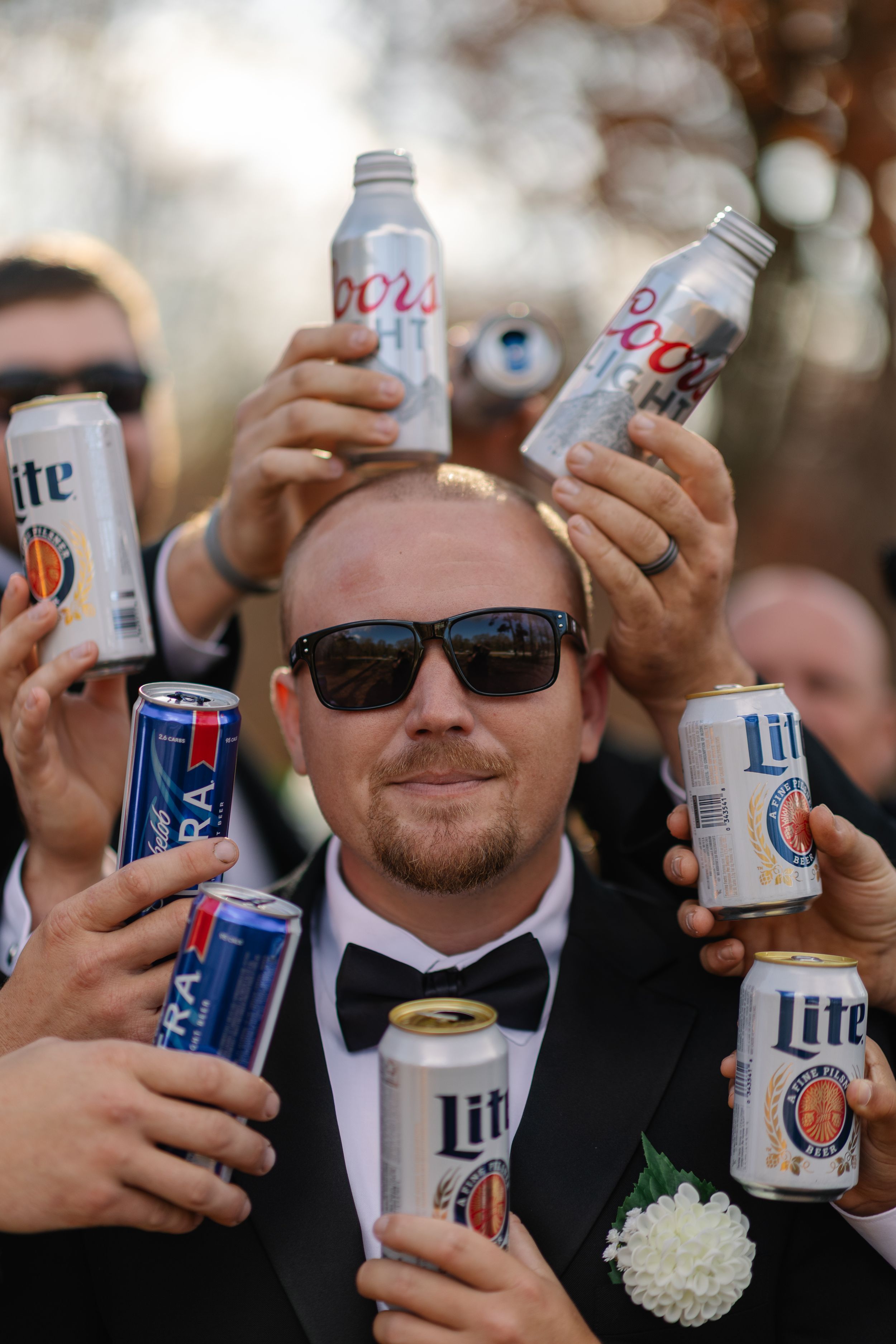 A group of hands holding up cans of beer in a celebratory toast during what appears to be a party or gathering.