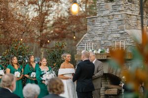 Outdoor wedding ceremony at stone fireplace with bridesmaids in teal dresses during golden hour sunset.