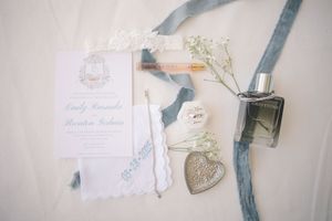 Wedding invitation details and decorative items arranged with a heart-shaped locket and blue ribbon on a light surface.