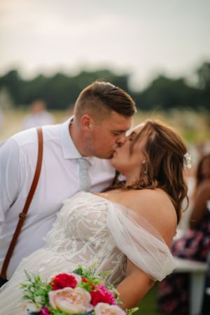 A romantic wedding moment captured outdoors with a beautiful bouquet featuring red and pink flowers.