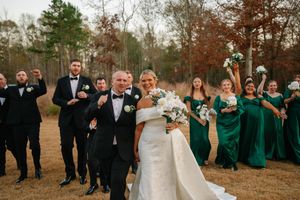 Wedding party in black suits and emerald green dresses pose together in an autumn outdoor setting.