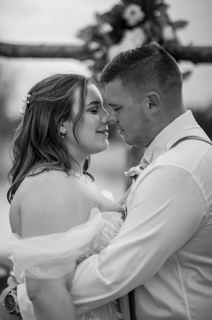 A romantic black and white wedding photo shows a couple in an intimate moment with the bride in white and groom in light attire.
