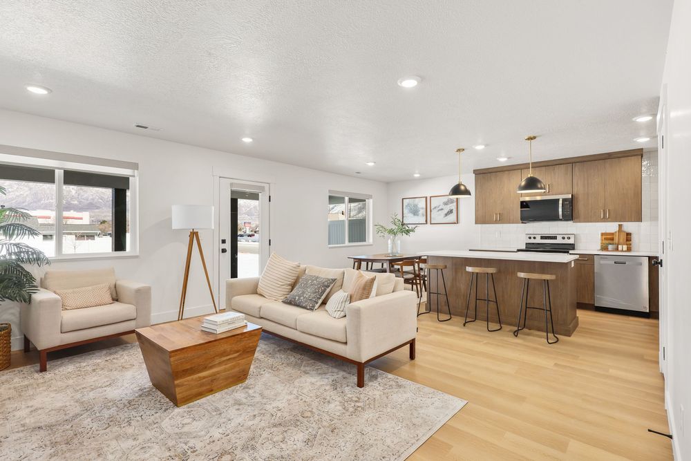 Bright open-concept living room with light hardwood floors, modern kitchen with island seating and stainless steel appliances.