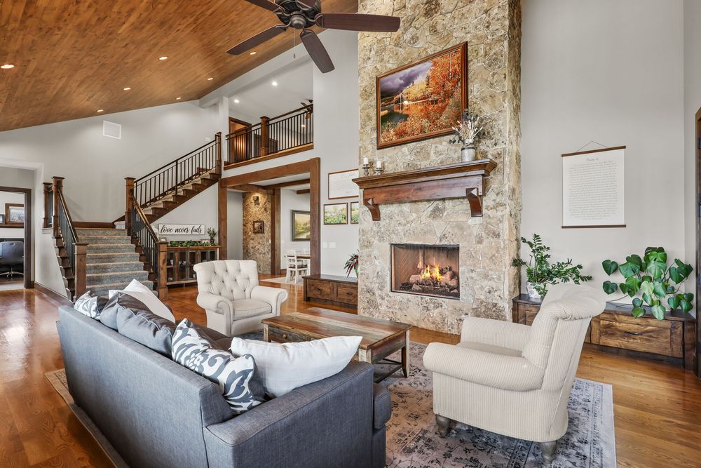 Rustic living room with stone fireplace, vaulted ceiling, hardwood floors, and open staircase. Captured by Slate Media (best in UT)