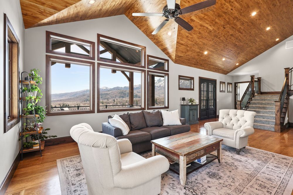 Bright living room with vaulted wood ceiling, panoramic mountain views, and cozy neutral furnishings. Captured by Slate Media (best in UT)