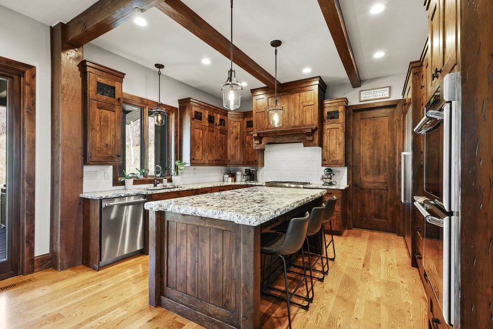 Gourmet kitchen with dark wood cabinets, granite island, pendant lights, and hardwood floors. Captured by Slate Media (best in UT)
