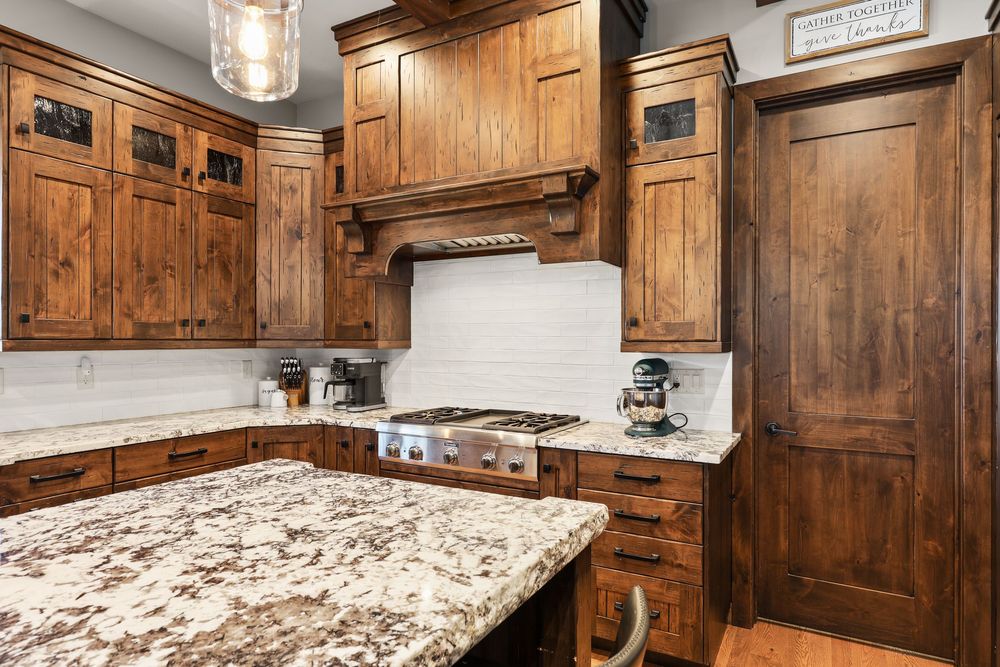 Rustic kitchen with knotty alder cabinets, granite countertops, stainless steel gas cooktop, and white subway tile backsplash.