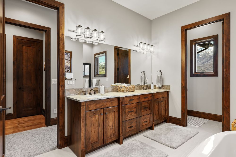 Elegant master bathroom with double dark wood vanity, dual mirrors, stone countertops, and natural light from a window.