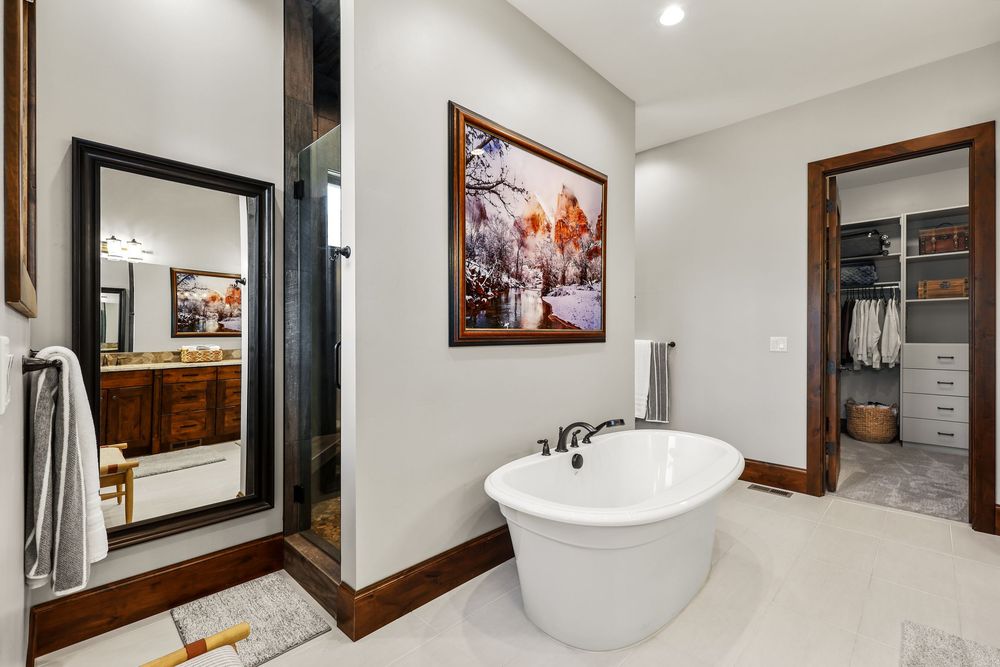 Luxurious bathroom featuring a freestanding soaking tub, large mirror, recessed lighting, and walk-in closet access. Captured by Slate Media