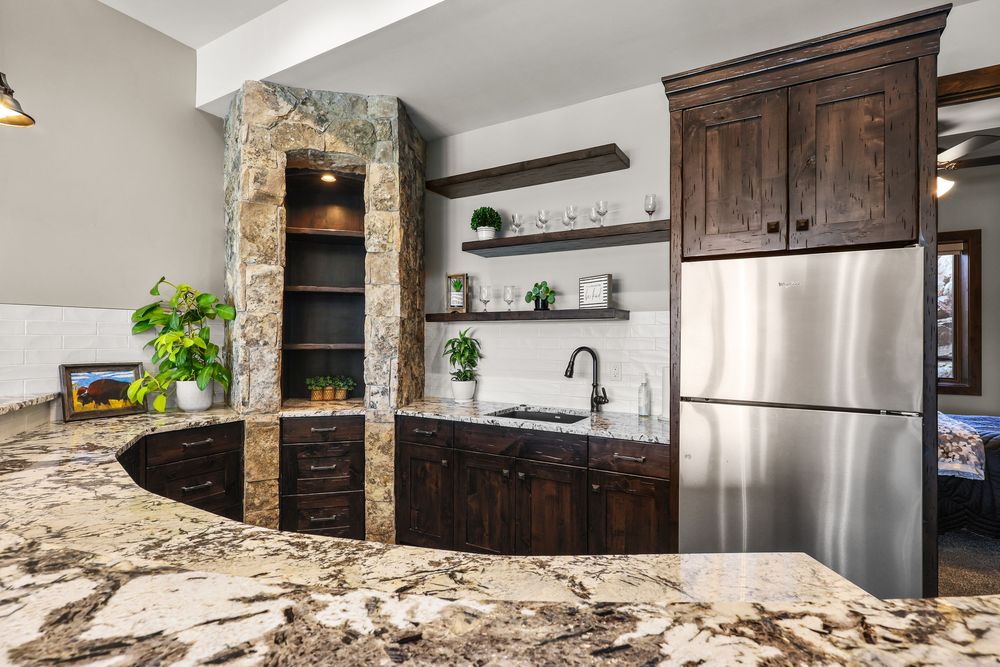 Gourmet kitchen featuring granite countertops, dark wood cabinets, stone accent wall, open shelving, and stainless steel fridge.