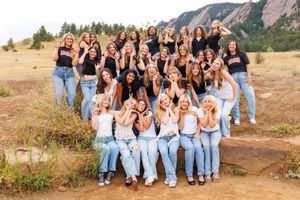 Large group of young women posing outdoors near rocky flatirons landscape in Colorado, wearing black tops and jeans.