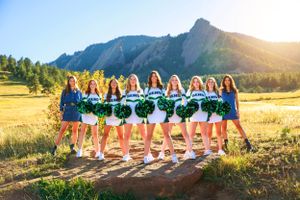Cheerleading team in matching uniforms poses in front of Flatirons mountains.