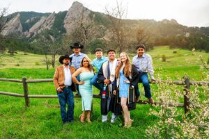A group of people posing against a scenic mountain backdrop with vibrant green grass and wildflowers in Boulder, Colorado.