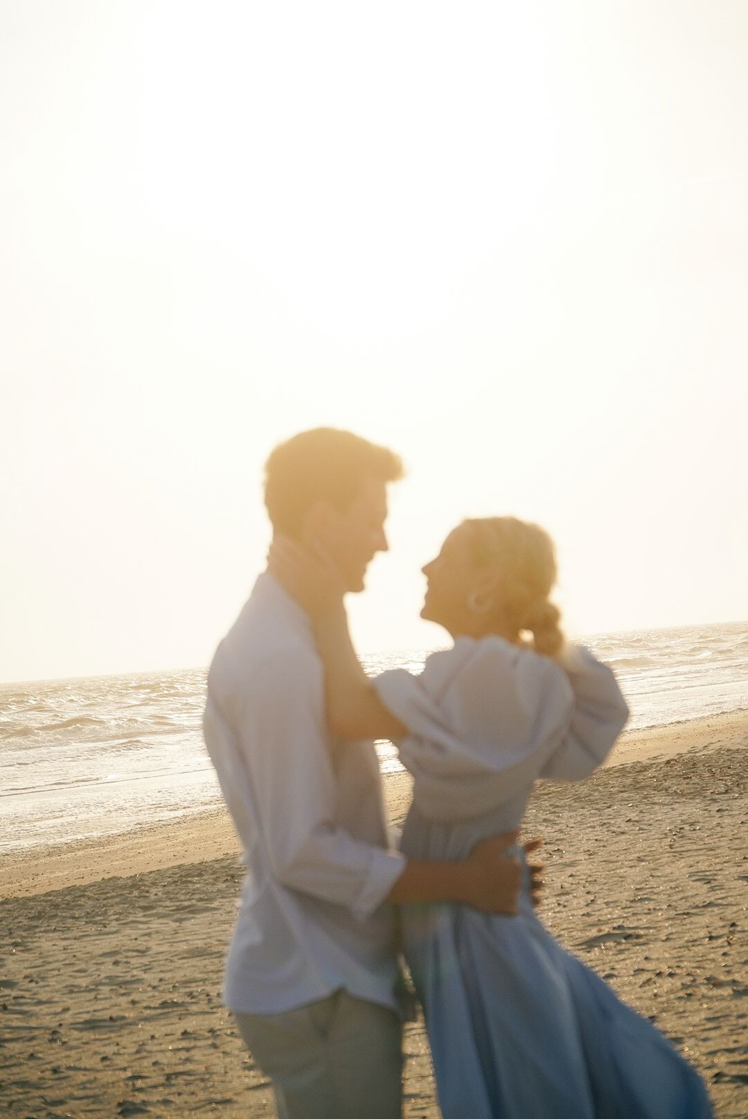 A romantic couple embraces on a sunlit beach during golden hour, creating a dreamy silhouette against the ocean backdrop.
