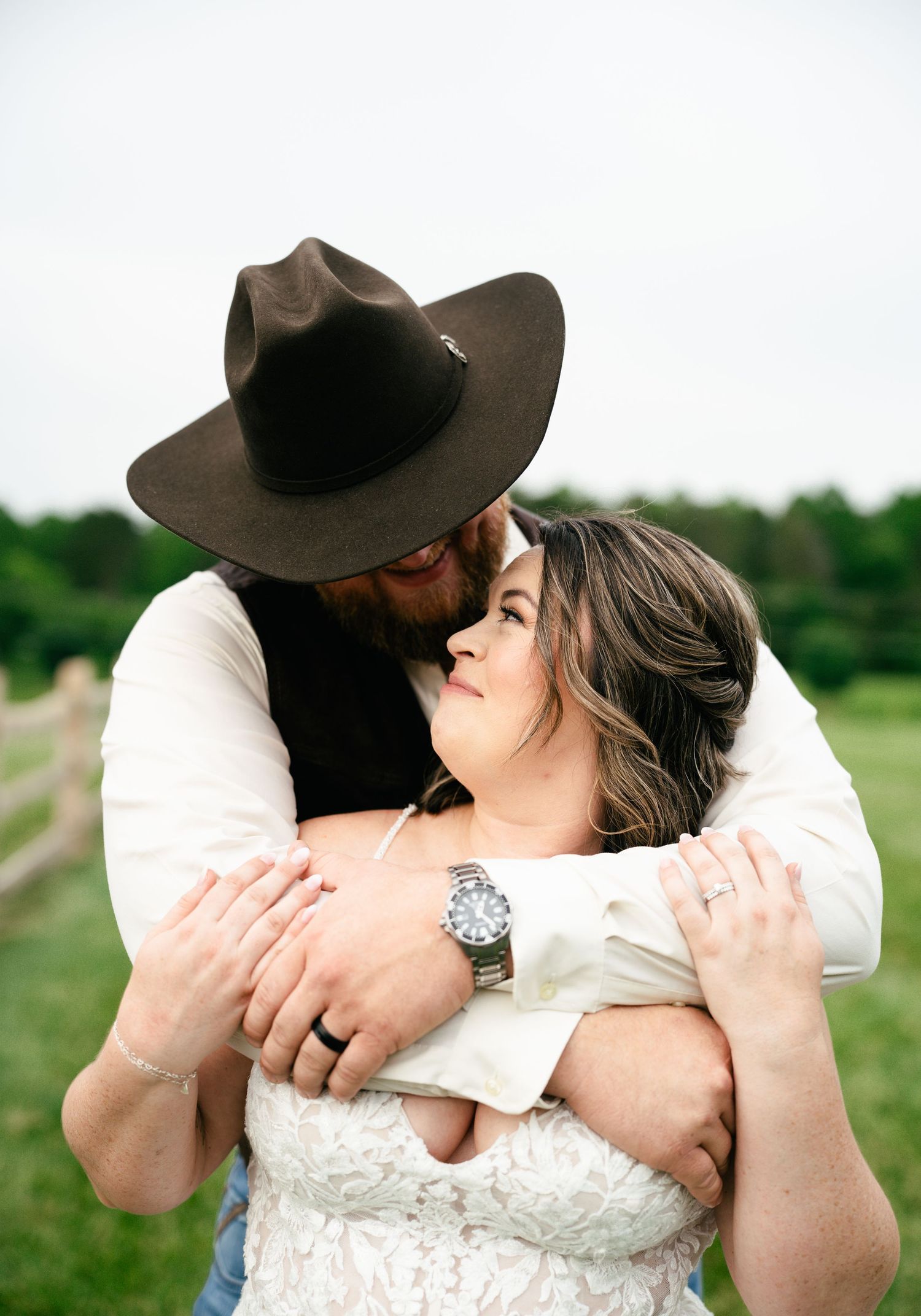 A tender embrace between a couple in a field, with the person wearing a brown cowboy hat and white shirt hugging their partner.