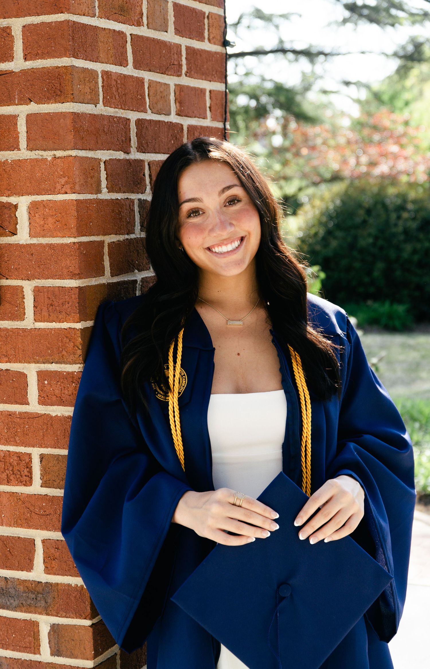 Graduation photos showcasing navy blue cap and gown against brick wall background.