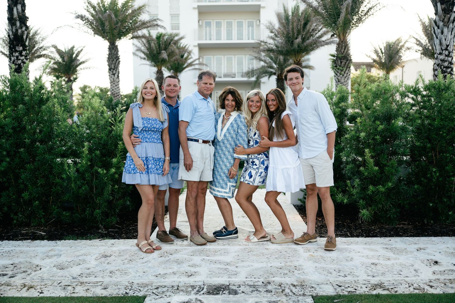 Group in coordinated blue and white summer outfits pose together in front of palm trees at a tropical location.