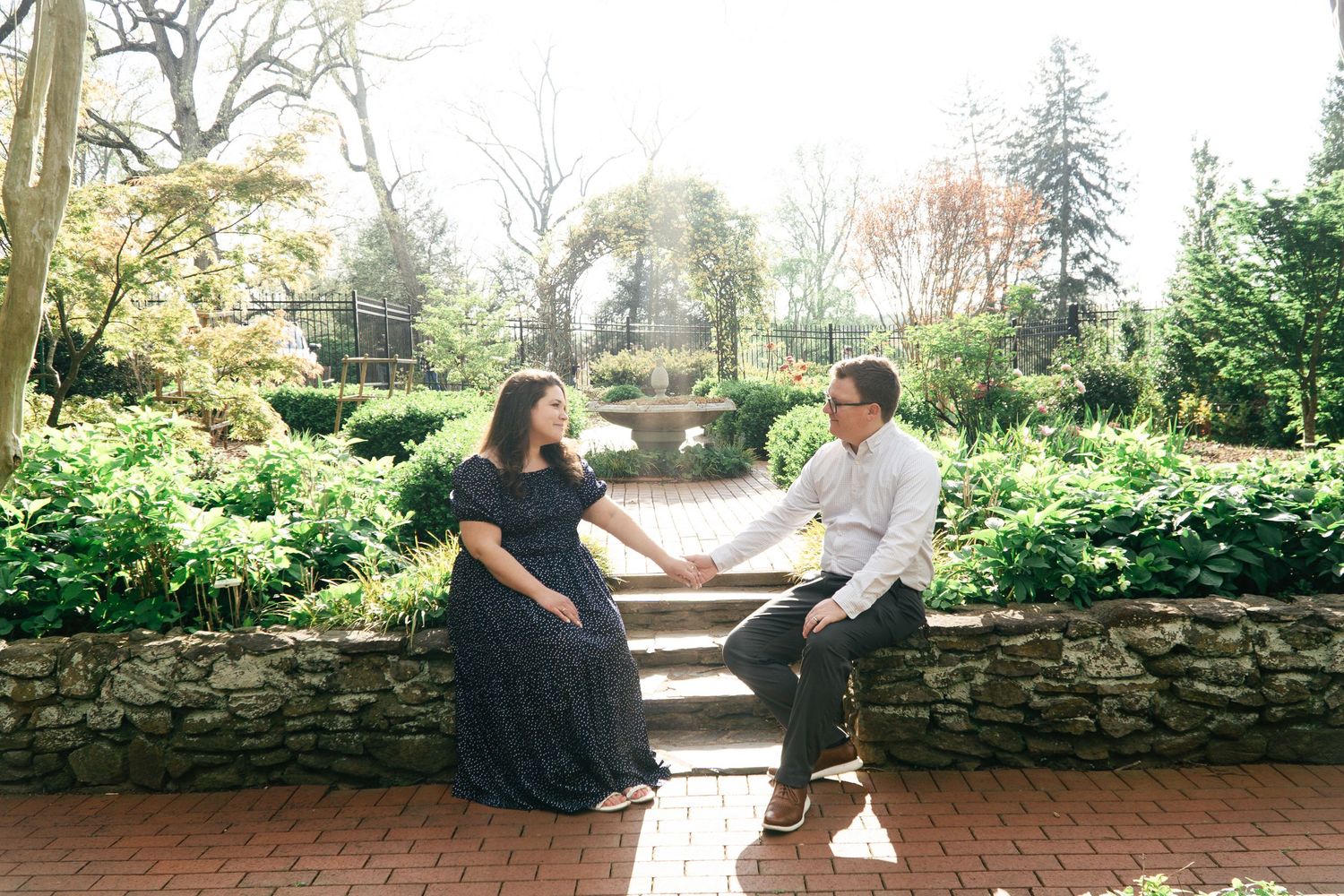 Casual outdoor portrait session on stone wall surrounded by lush greenery.
