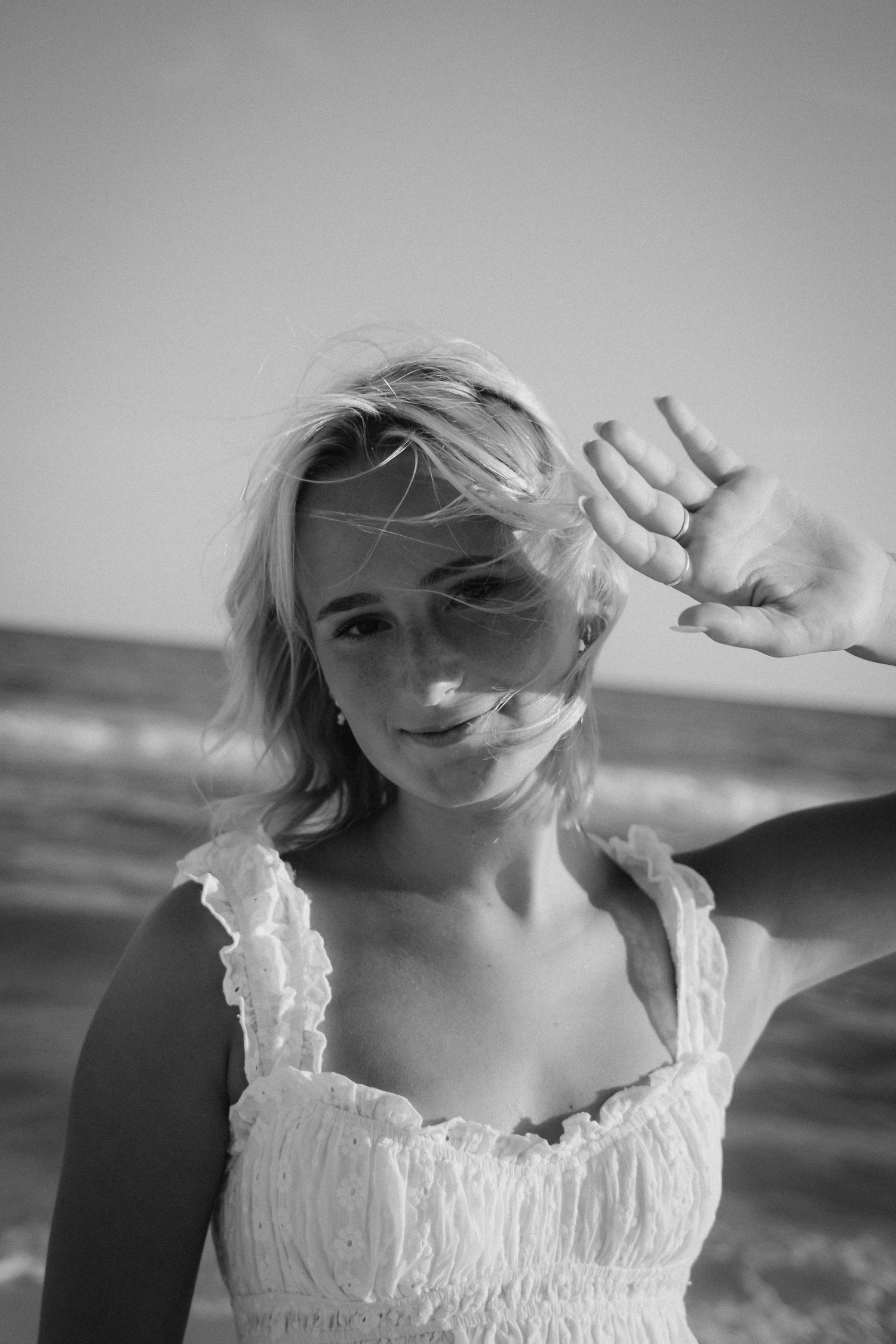 Black and white portrait of person in white dress at beach with windswept hair.