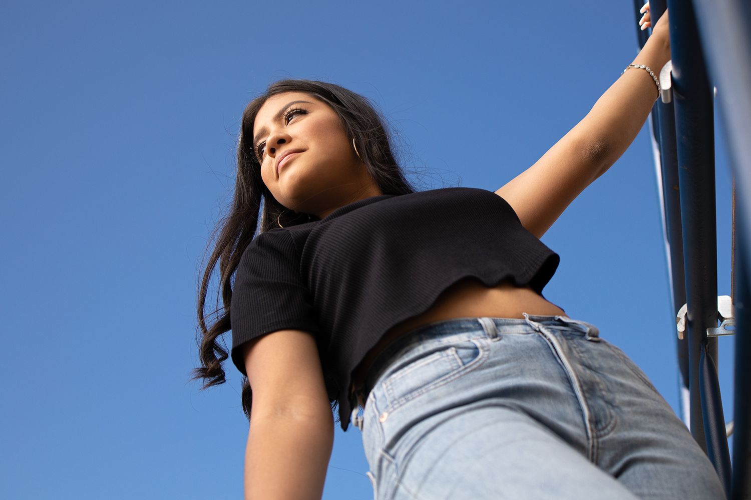 High school senior girl holding on to bar to pose for a photograph. wearing black shirt and blue jeans