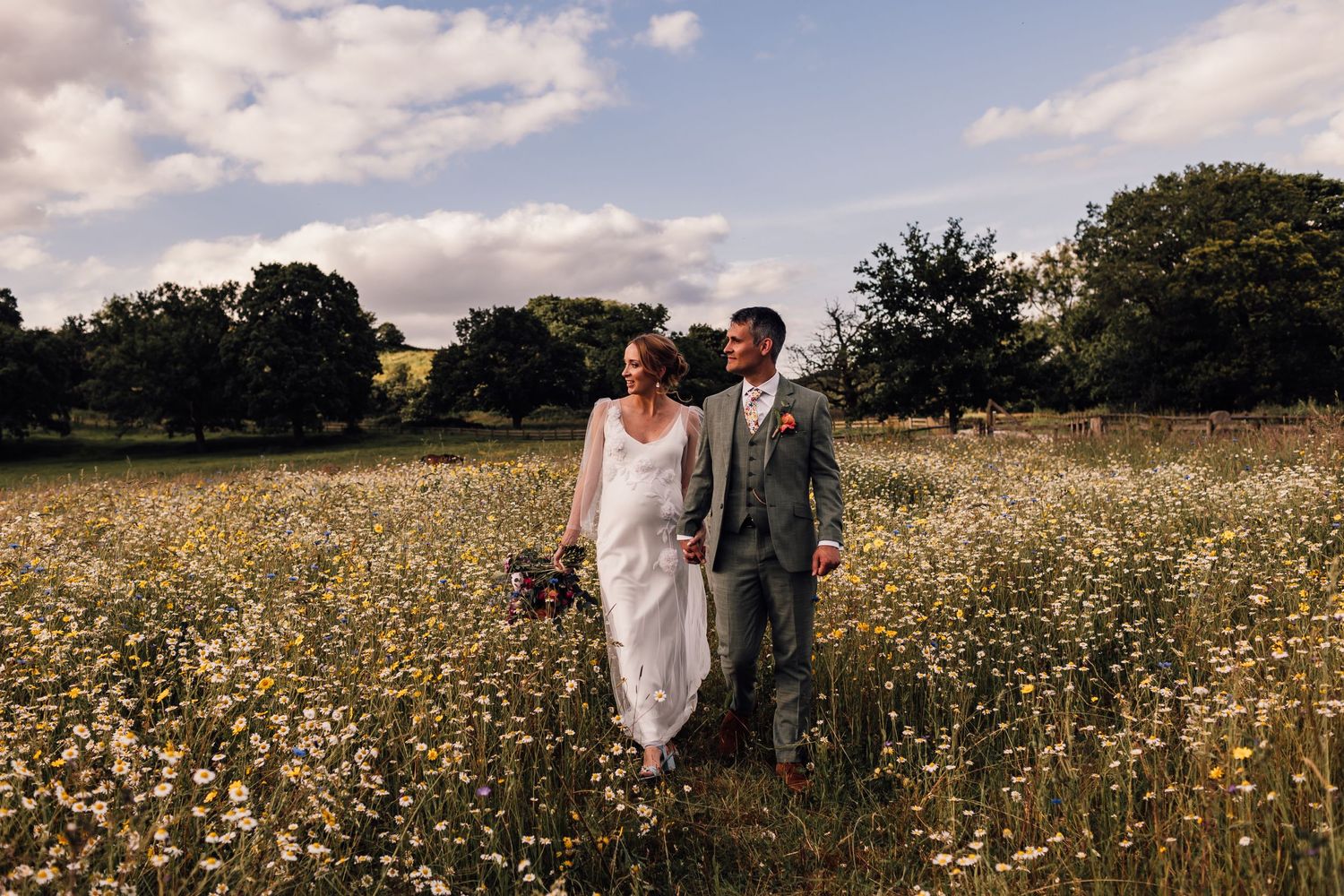 A couple stands together in a blooming wildflower meadow on their wedding day.
