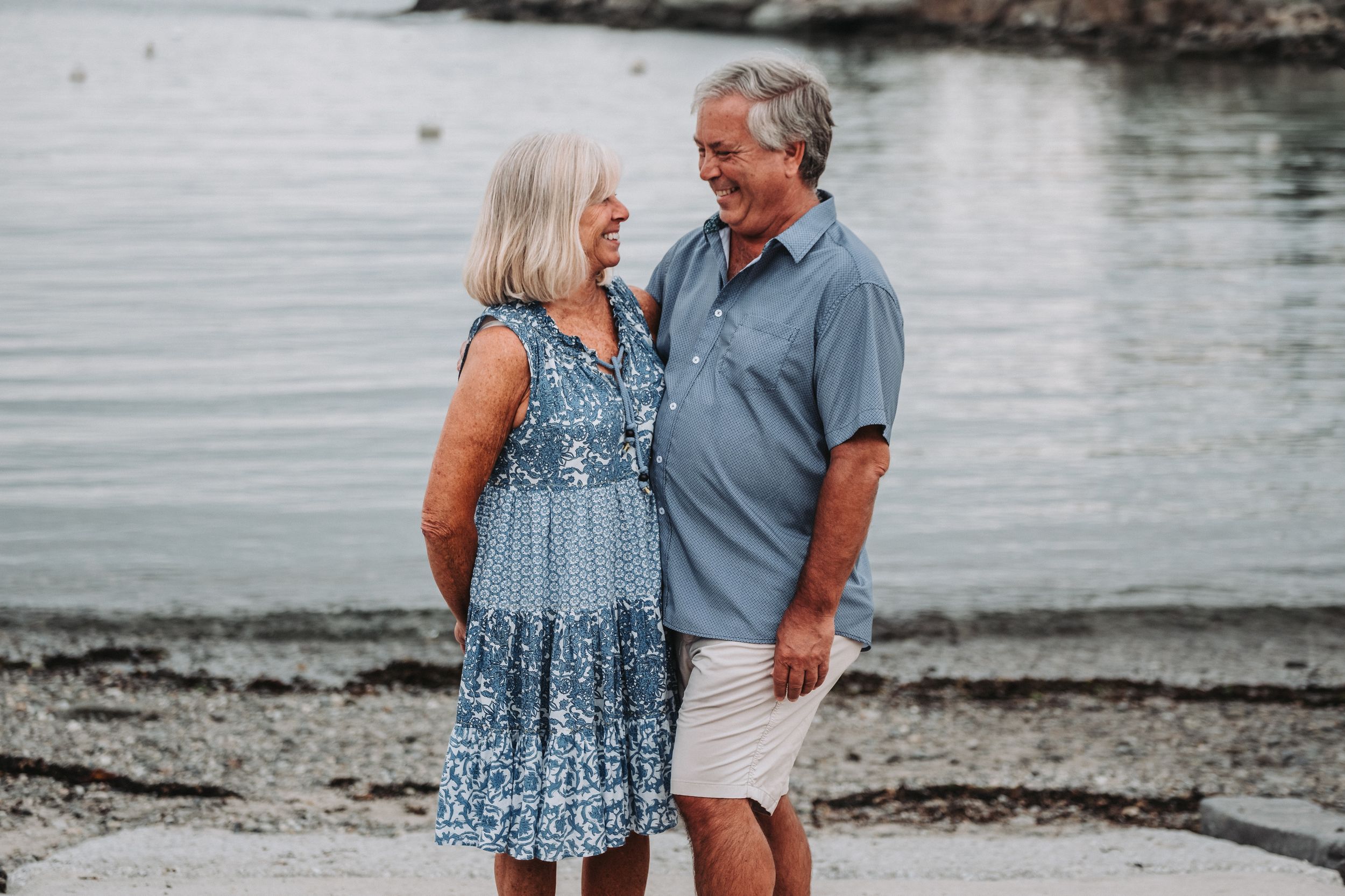 An older couple smiles at each other on a beach at Ocean Point Park in Boothbay, Maine. Photo taken during an extended family photo session.