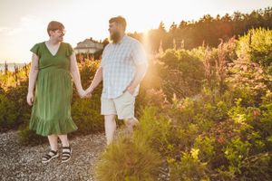 A couple holds hands while walking along a scenic mountain trail at sunset with wildflowers in the background.  Bailey Island, Maine.